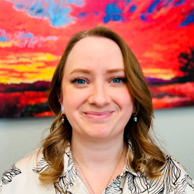 Portrait photo of Jordan with loose hair, and in the background a painting with reddish tones.